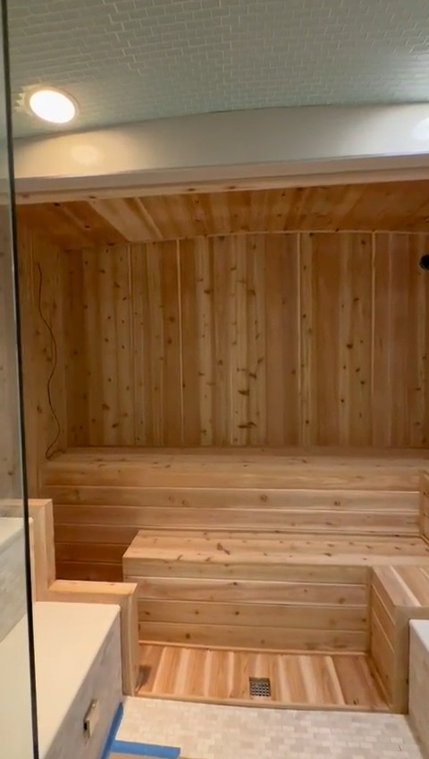 Through the glass door: knotty tongue-and-groove walls, chamfered ceiling, a two-tier bench and slatted floor with a drain